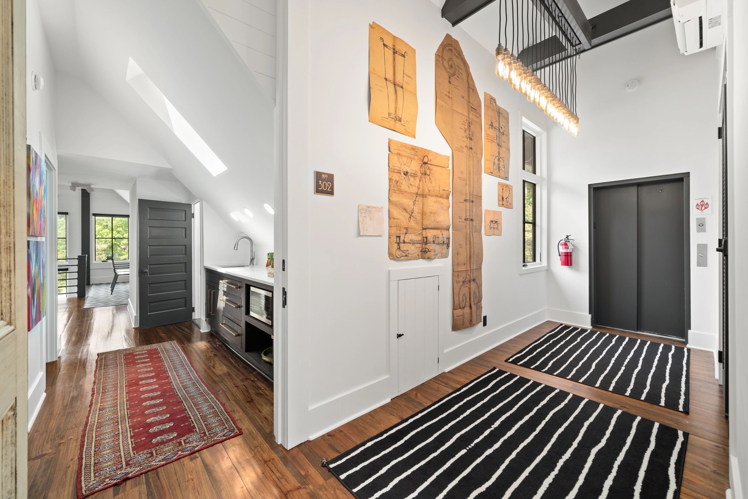 Modern hallway with wood floors, black elevator doors, and striped rugs